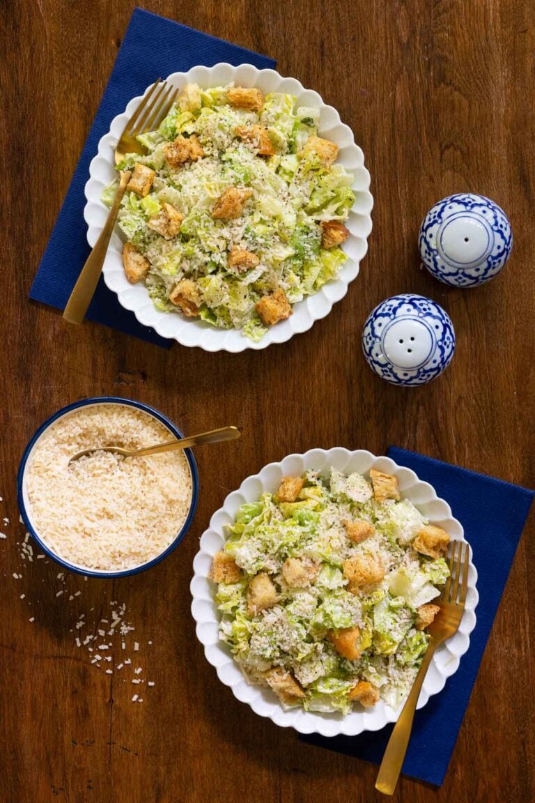Caesar Salads on white plates with a bowl of dressing.