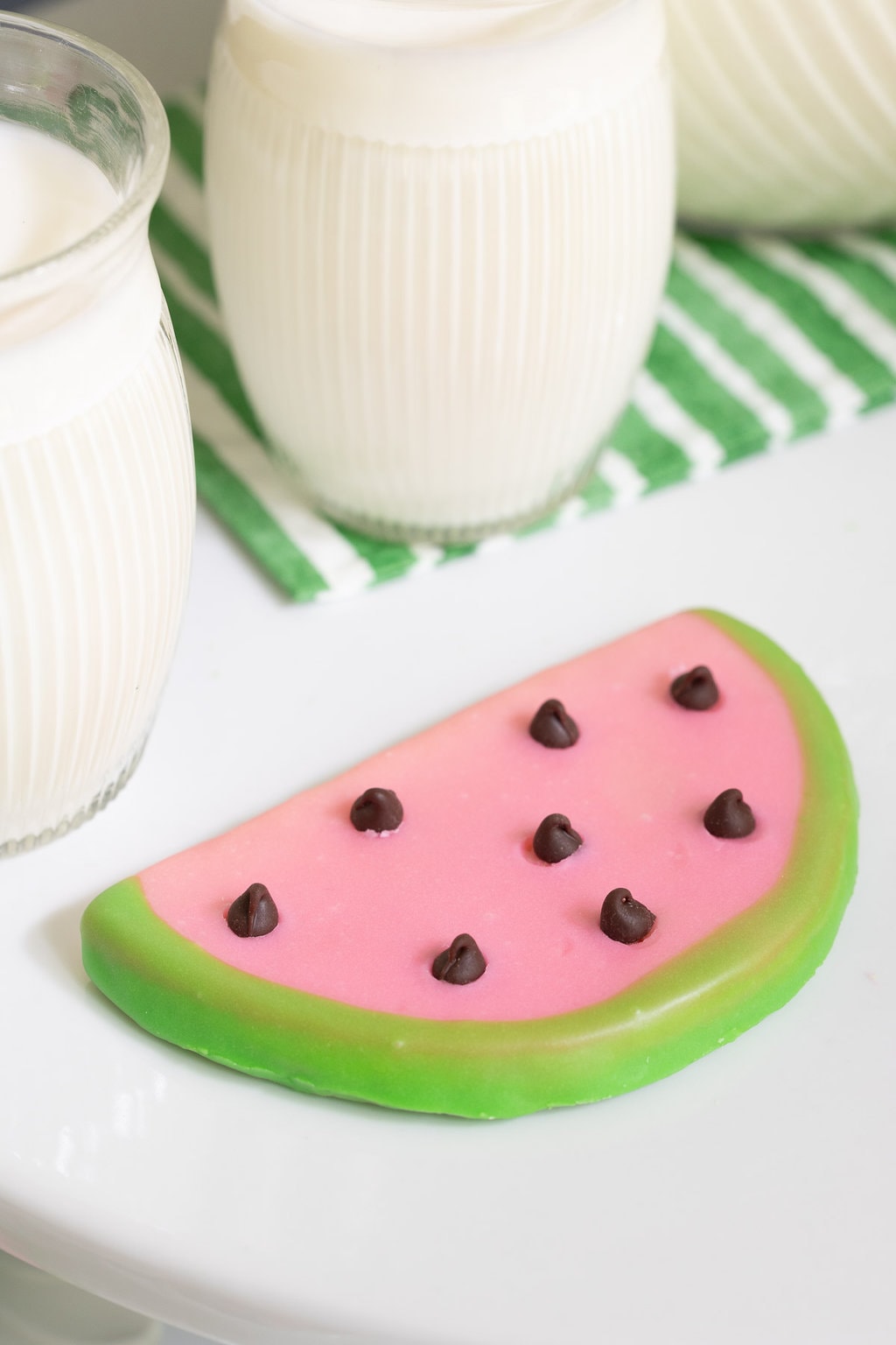 Vertical closeup photo of a Watermelon Shortbread Cookie surrounded by glasses of milk.