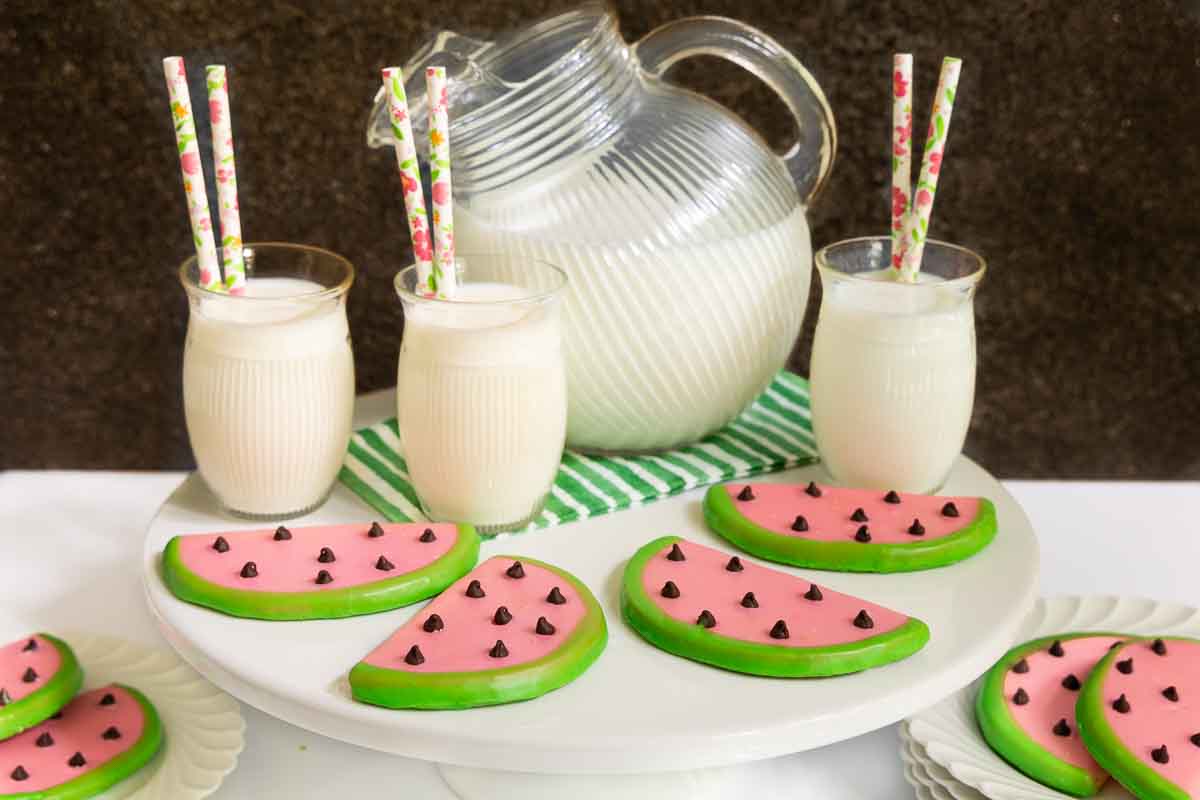Horizontal photo of a batch of Watermelon Shortbread Cookies surrounded by glasses of milk.