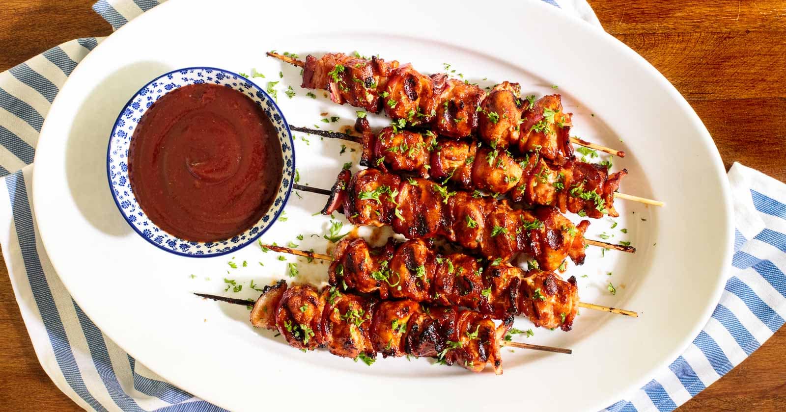 Horizontal overhead photo of Barbecued Bacon Bourbon Chicken Skewers on a white oval platter.