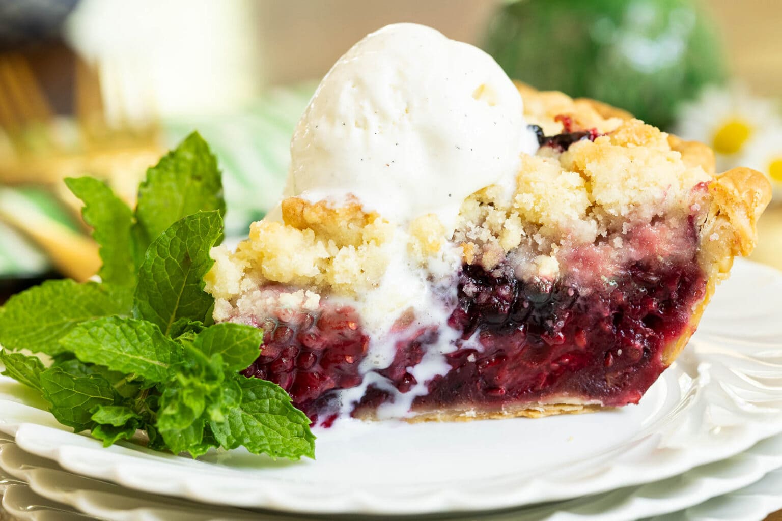Easy Blackberry Crumble Pie - thecafesucrefarine.com Horizontal extreme closeup photo of a slice of Easy Blackberry Crumble Pie with a scoop of ice cream melting on the top and a sprig of mint.