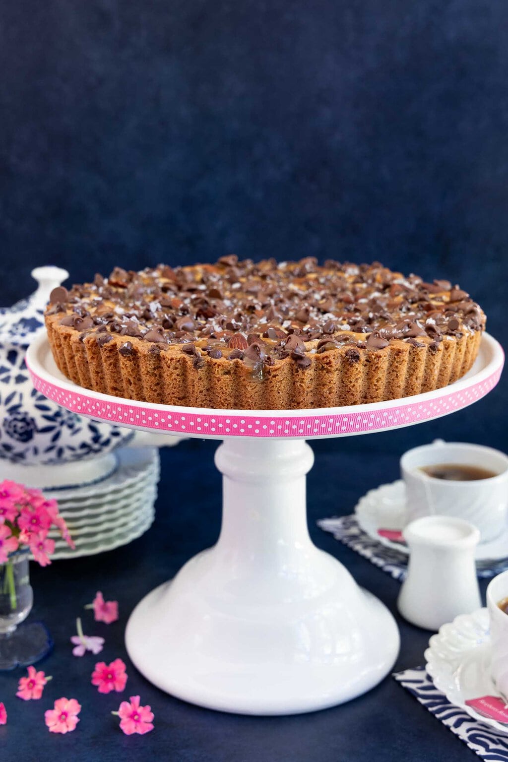 Vertical photo of an Easy Ritz Paris Cookie Tart on a white pedestal serving plate banded with pink ribbon with polka dots.