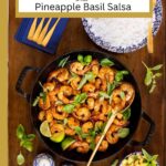 Vertical overhead photo of a black cast iron skillet pan of Vietnamese Caramel Shrimp. Bowls of rice and Pineapple Basil Salsa are nearby.