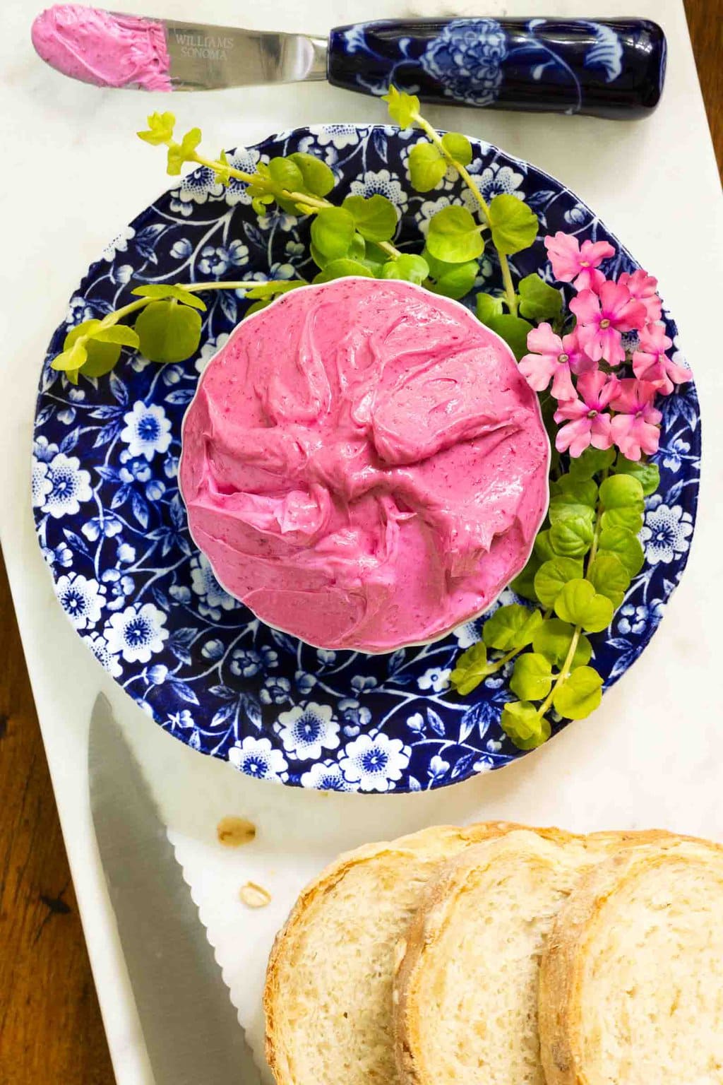 Vertical overhead closeup photo of Beet Butter on a blue and white patterned plate surrounded by greenery.