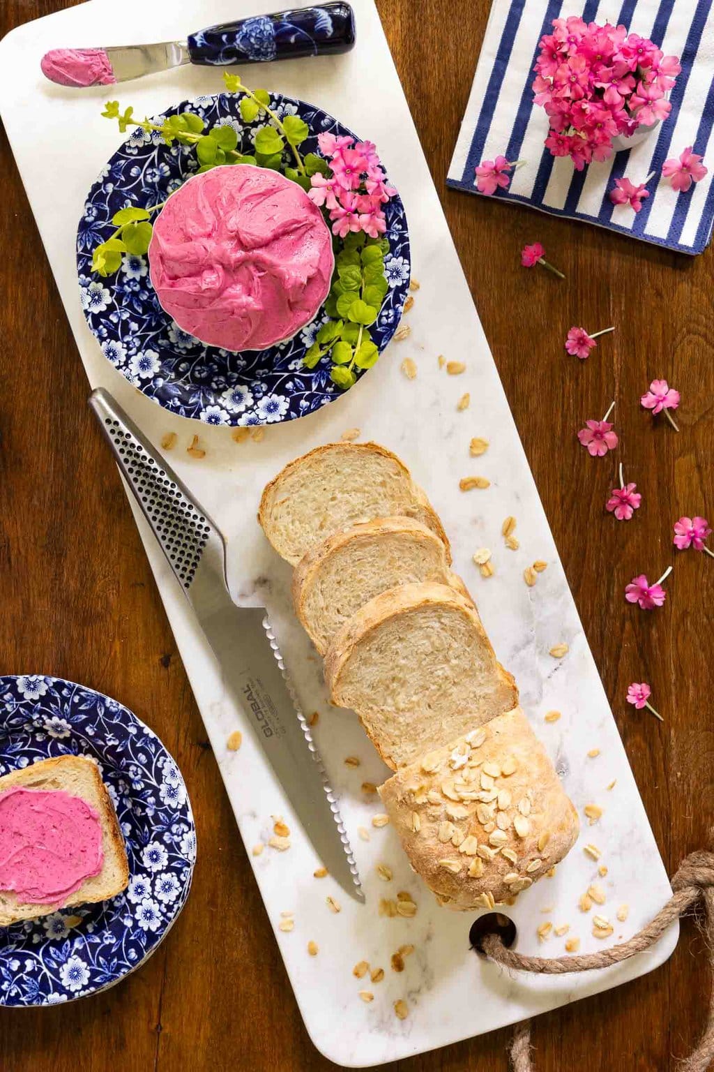 Vertical overhead photo of a sliced loaf of No-Knead Porridge Bread and a dish of Beet Butter on a blue and white patterned plate.