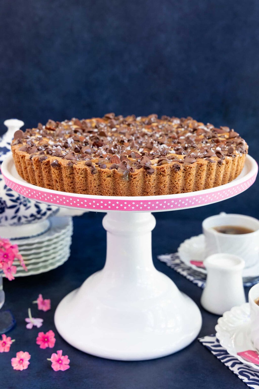 Vertical photo of a The Paris Ritz Cookie Tart on a white pedestal serving stand banded in pink ribbon with white polka dots.