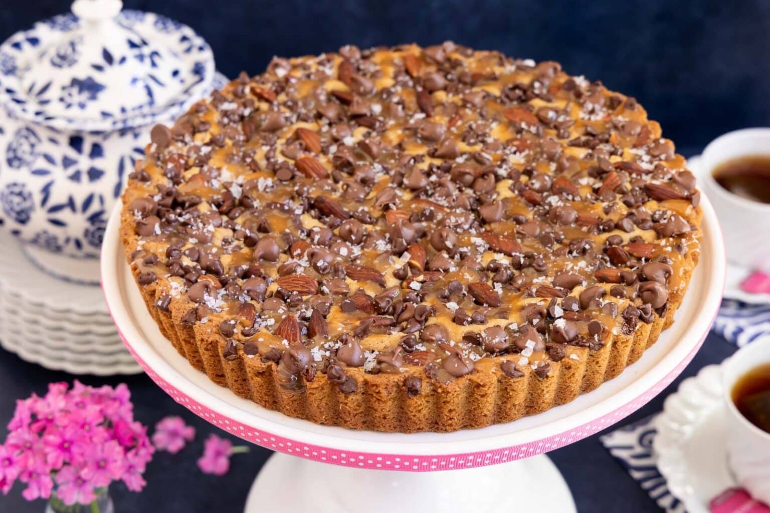 Horizontal photo of an Easy Ritz Paris Cookie Tart on a white pedestal serving plate banded with pink ribbon with polka dots.