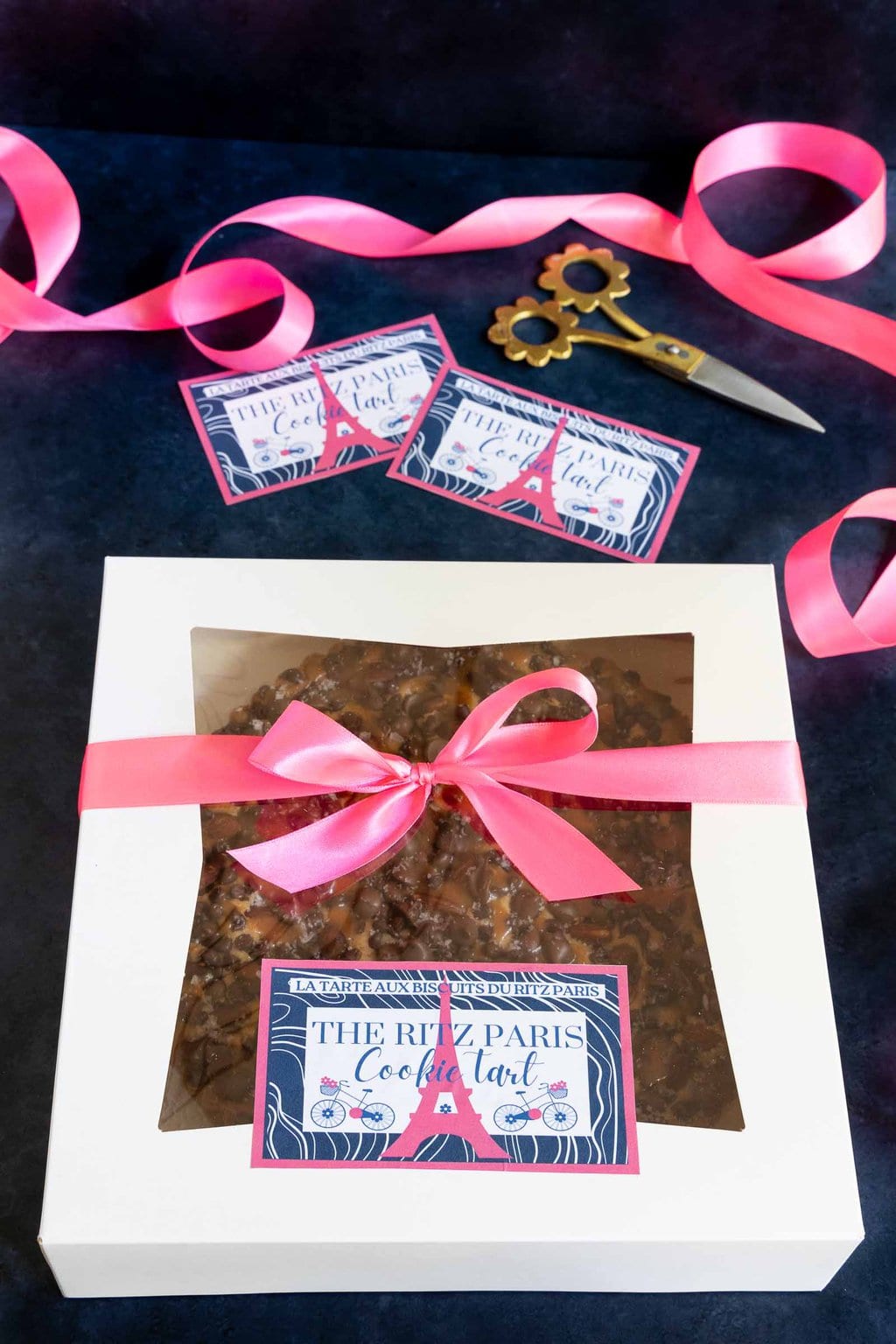 Vertical photo of a white window box with a Easy Ritz Paris Cookie Tart decorated with pink ribbon and a custom label for gift giving.