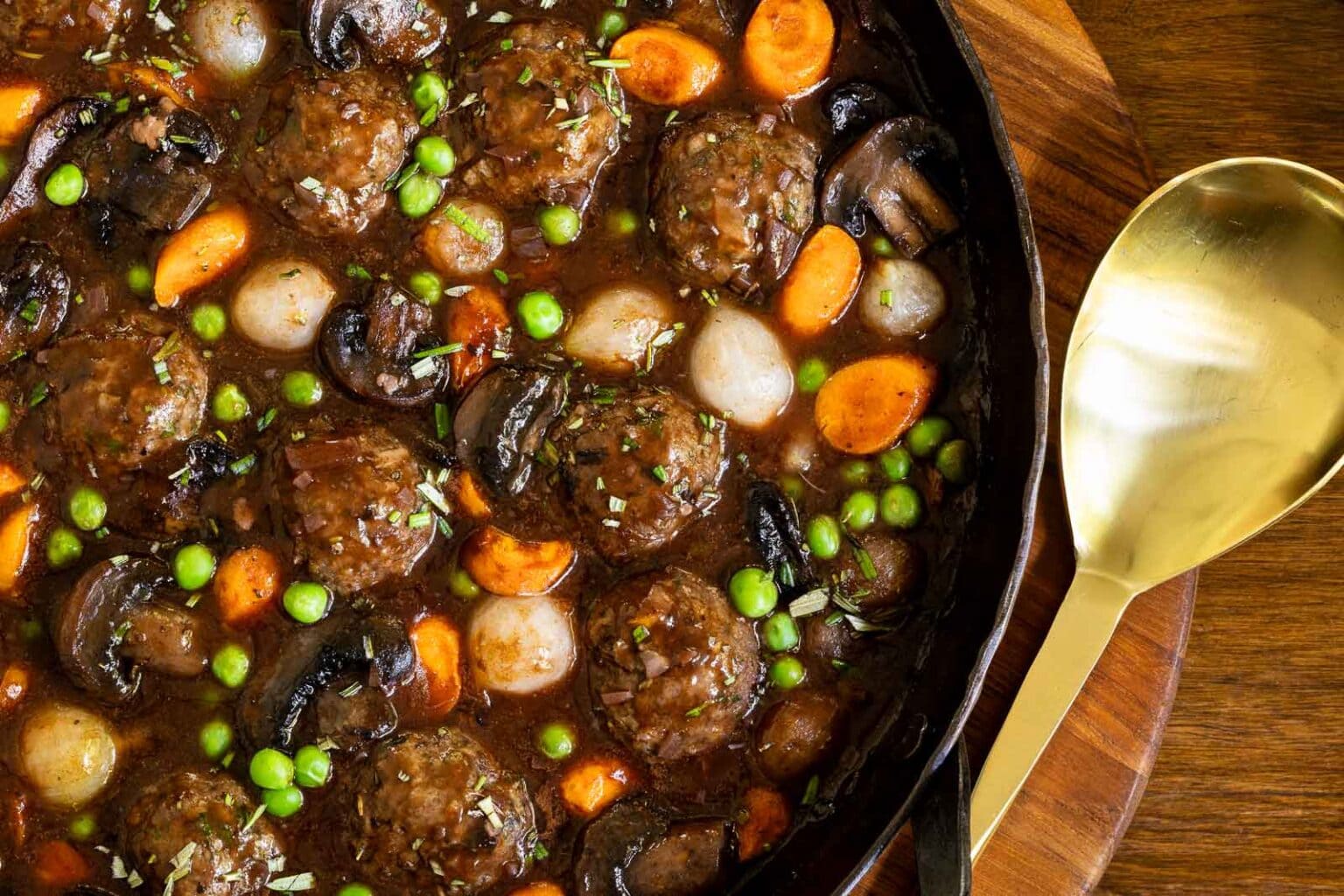 Horizontal overhead closeup photo of a cast iron skillet of Beef Bourguinon Meatballs (Boulettes de Bœuf Bourguignon).