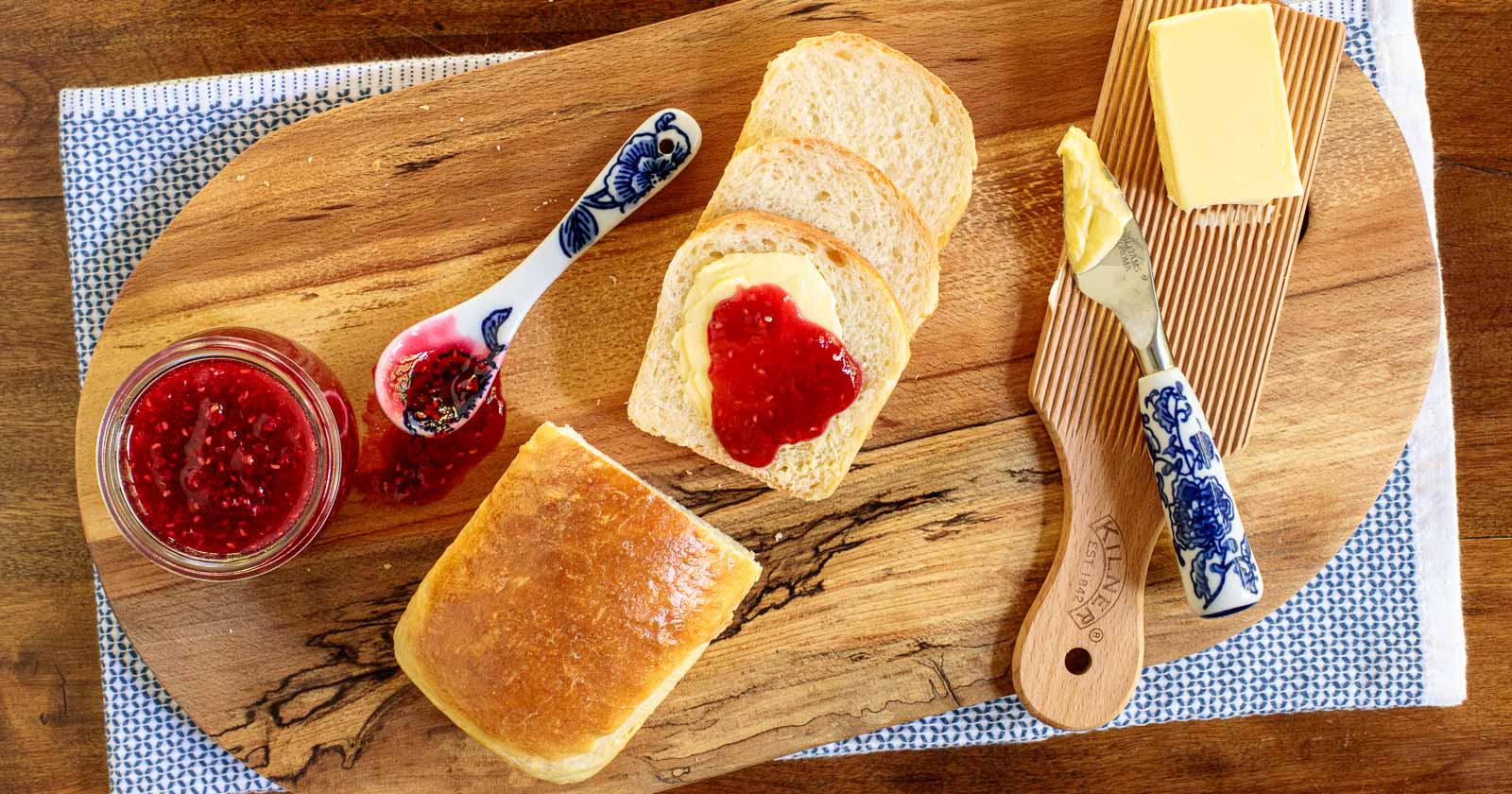 Horizontal overhead photo of homemade brioche bread on a wood cutting board with raspberry jam and fresh butter.