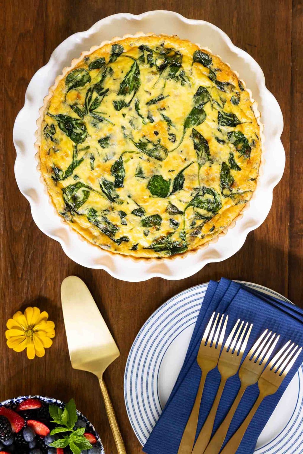 Vertical overhead photo of a French Bistro Spinach Quiche on a white scalloped serving plate on a wood table.