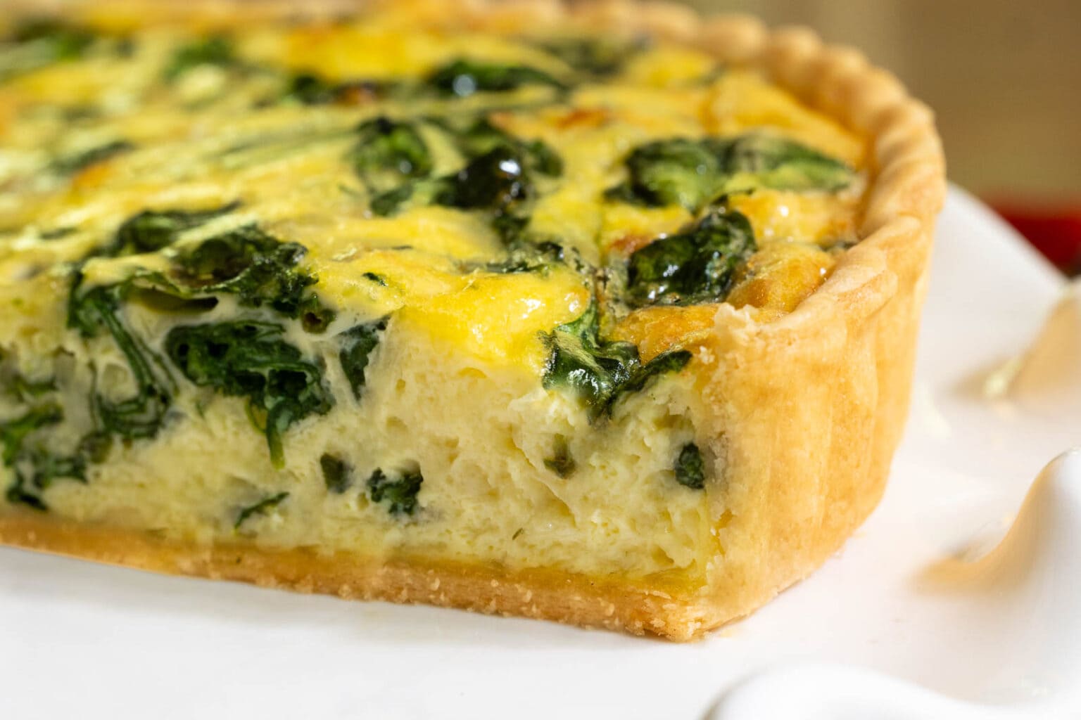 Horizontal extreme closeup of a piece of French Bistro Spinach Quiche on a white serving plate.