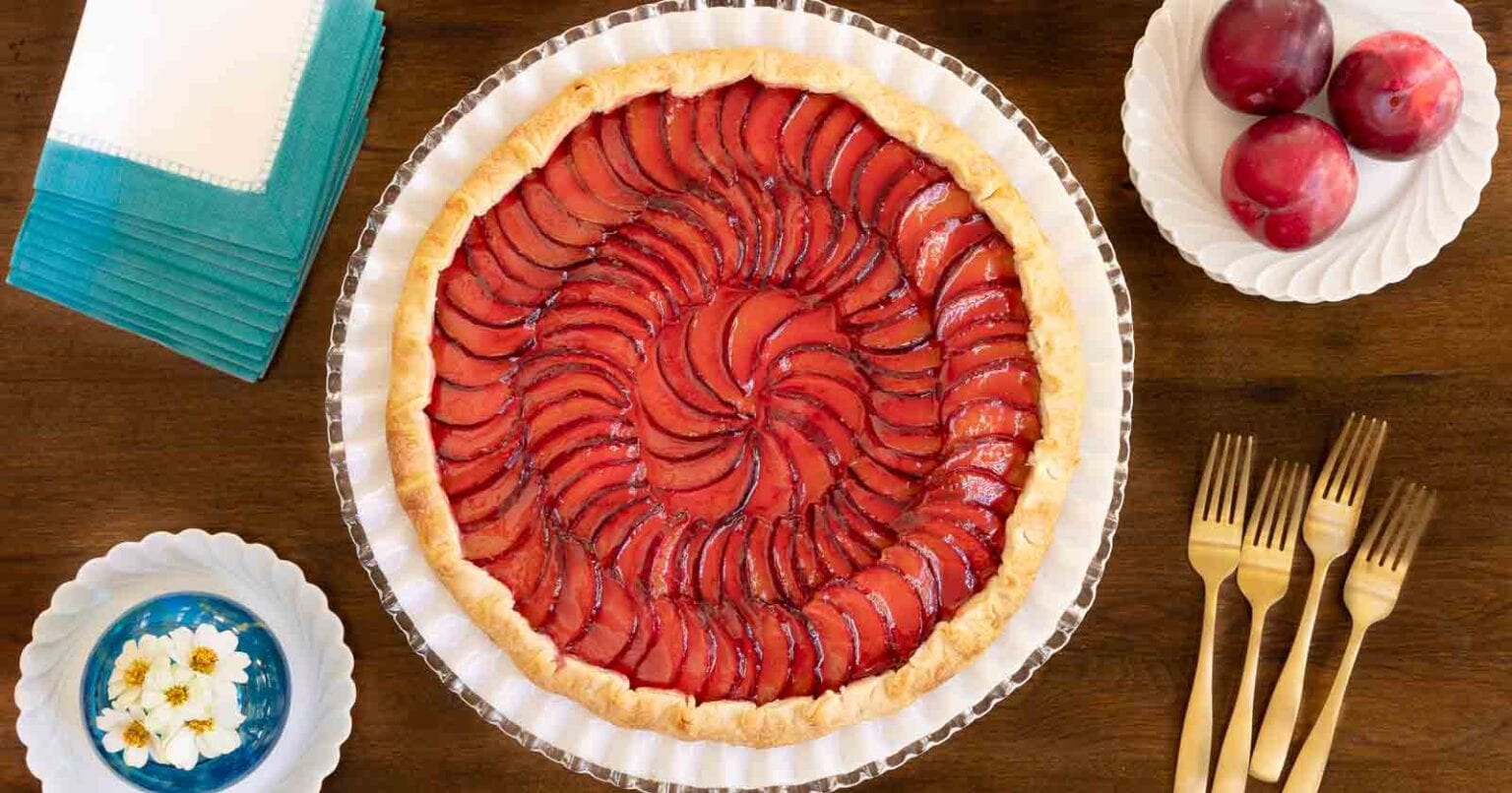 Ridiculously Easy French Plum Galette - thecafesucrefarine.com Horizontal overhead photo of a Ridiculously Easy French Plum Galette on a white glass serving plate on a wood table.