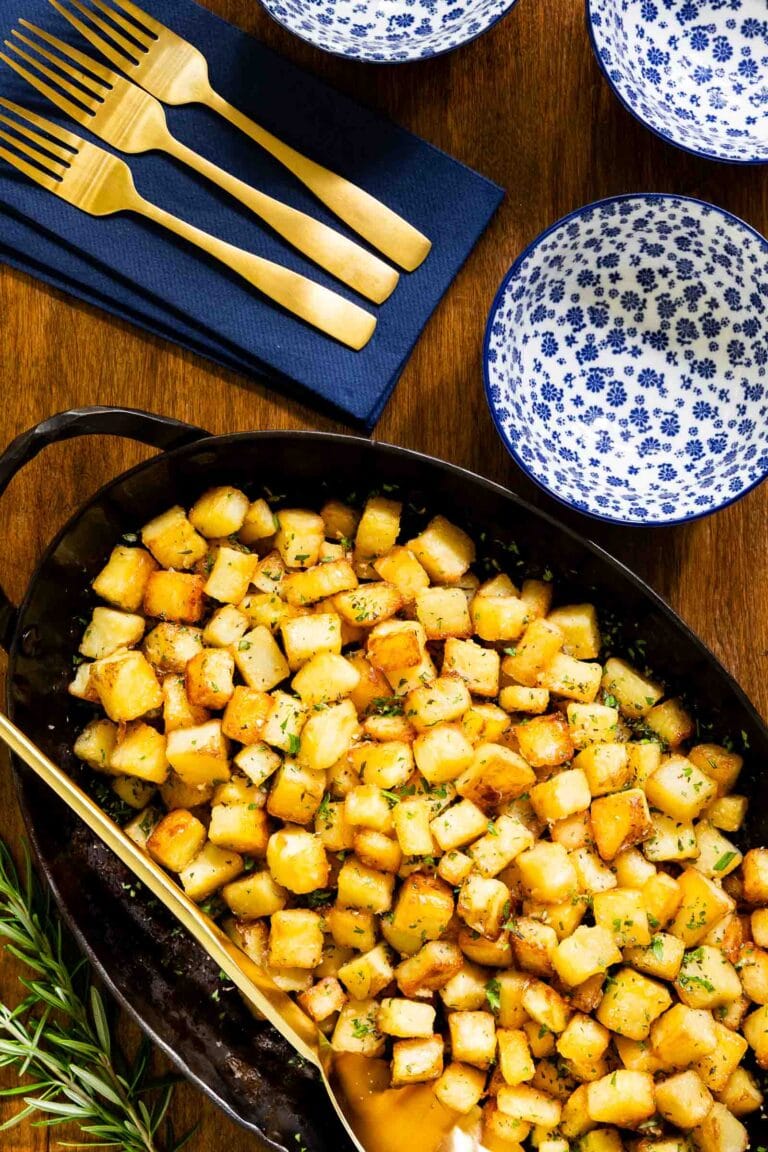Rosemary Roasted Parmentier Potatoes in an oval cast iron skillet with blue and white plates and gold forks.