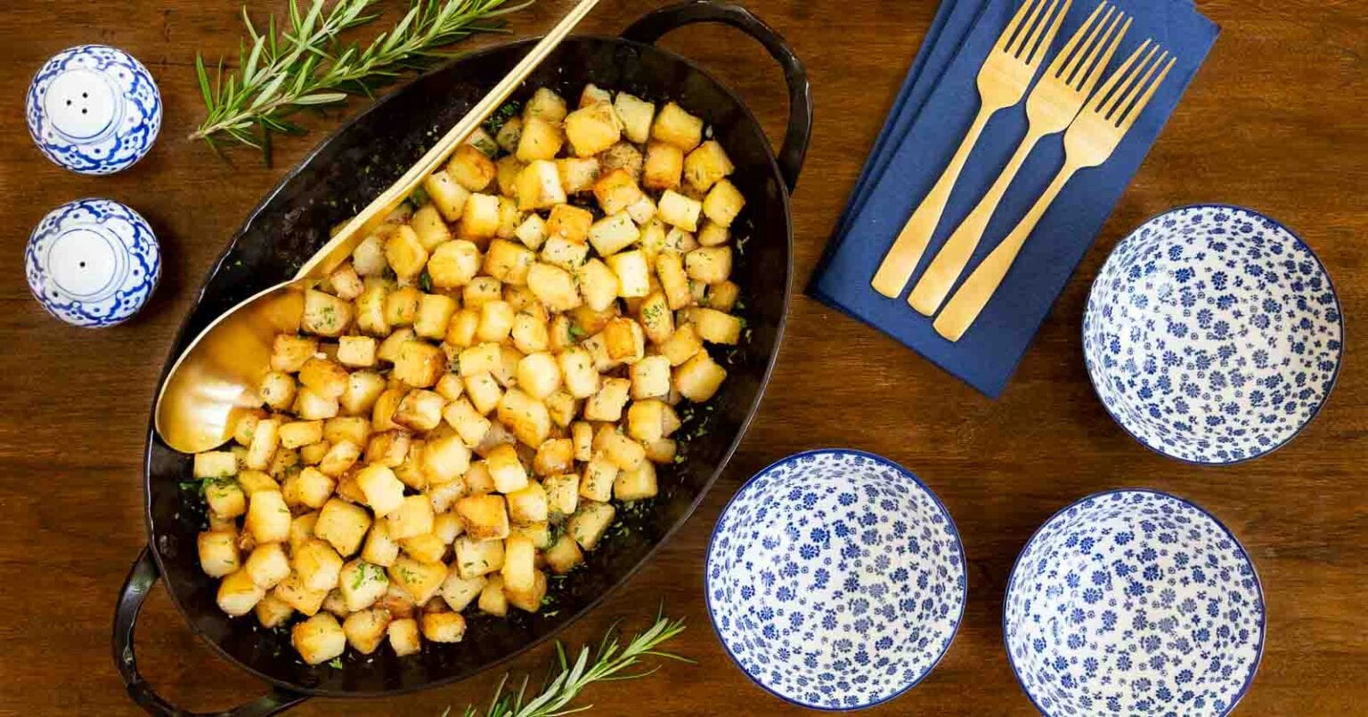 Rosemary Roasted French Parmentier Potatoes - thecafesucrefarine.com Horizontal overhead photo of an oval steel skillet of Rosemary Roasted French Parmentier Potatoes on a wood table.