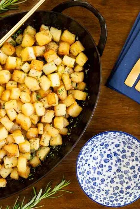 Horizontal overhead photo of a hammered steel pan of Rosemary Roasted French Parmentier Potatoes on a wood table.