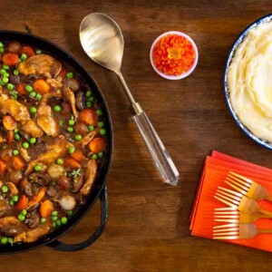 Horizontal overhead photo of a cast iron skillet of Easy, Make-Ahead Parisian Coq au Vin with a side of mashed potatoes.
