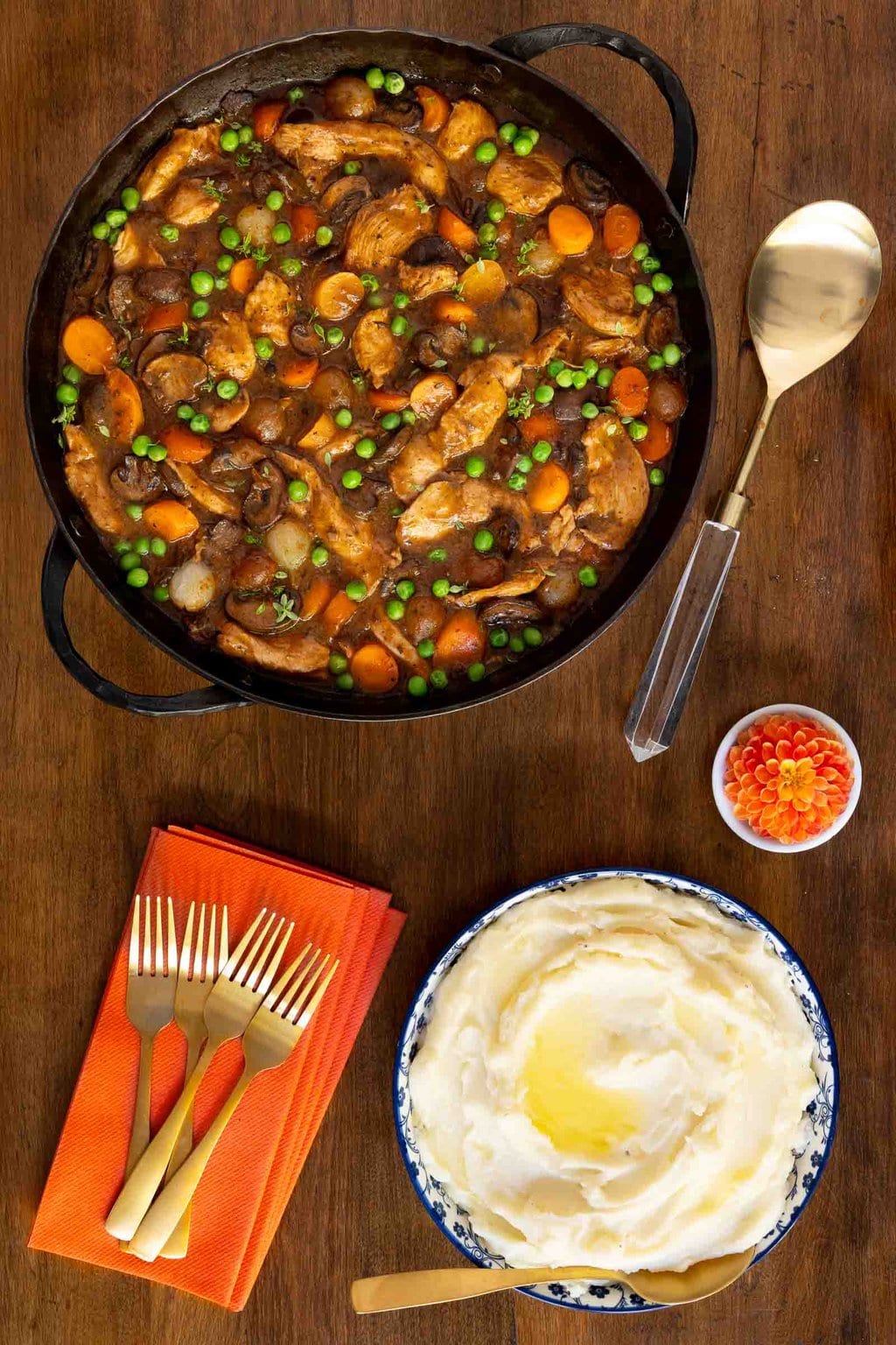 Vertical overhead photo of a cast iron skillet of Easy, Make-Ahead Parisian Coq au Vin on a wood table with a side of mashed potatoes.
