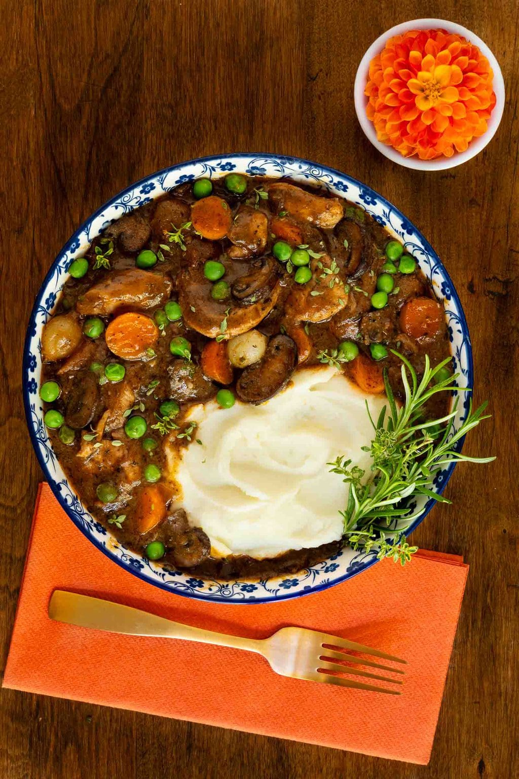 Vertical overhead photo of a serving bowl of Easy, Make-Ahead Parisian Coq au Vin with a side of mashed potatoes and garnished with rosemary.