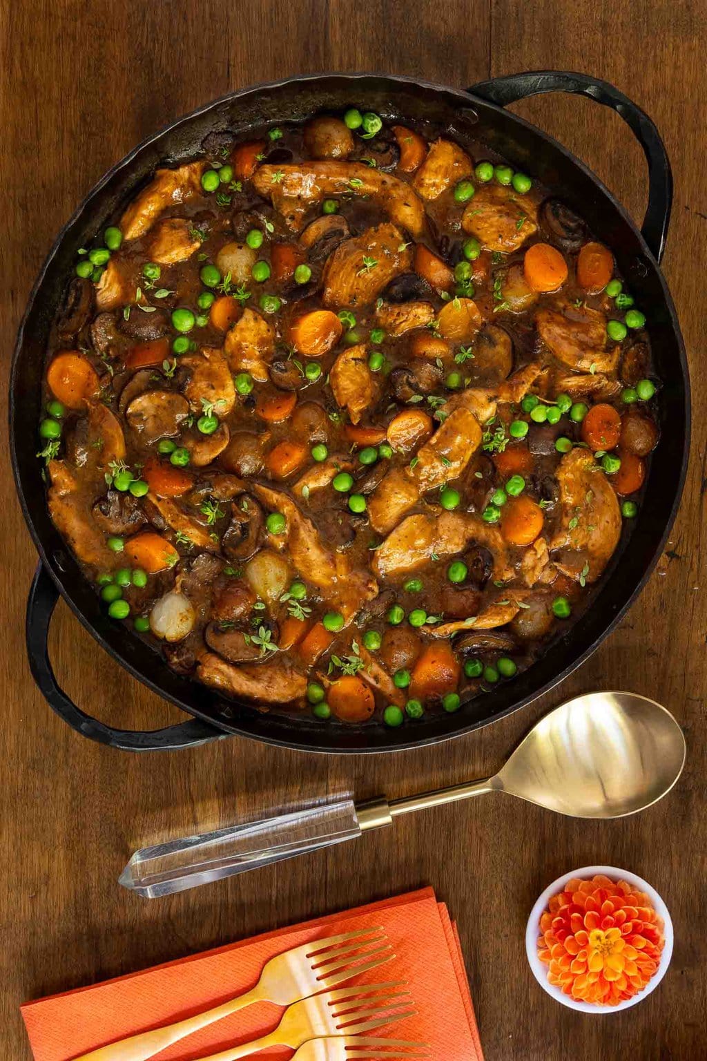 Vertical overhead photo of a black cast iron skillet of Easy, Make-Ahead Parisian Coq au Vin on a wood table.