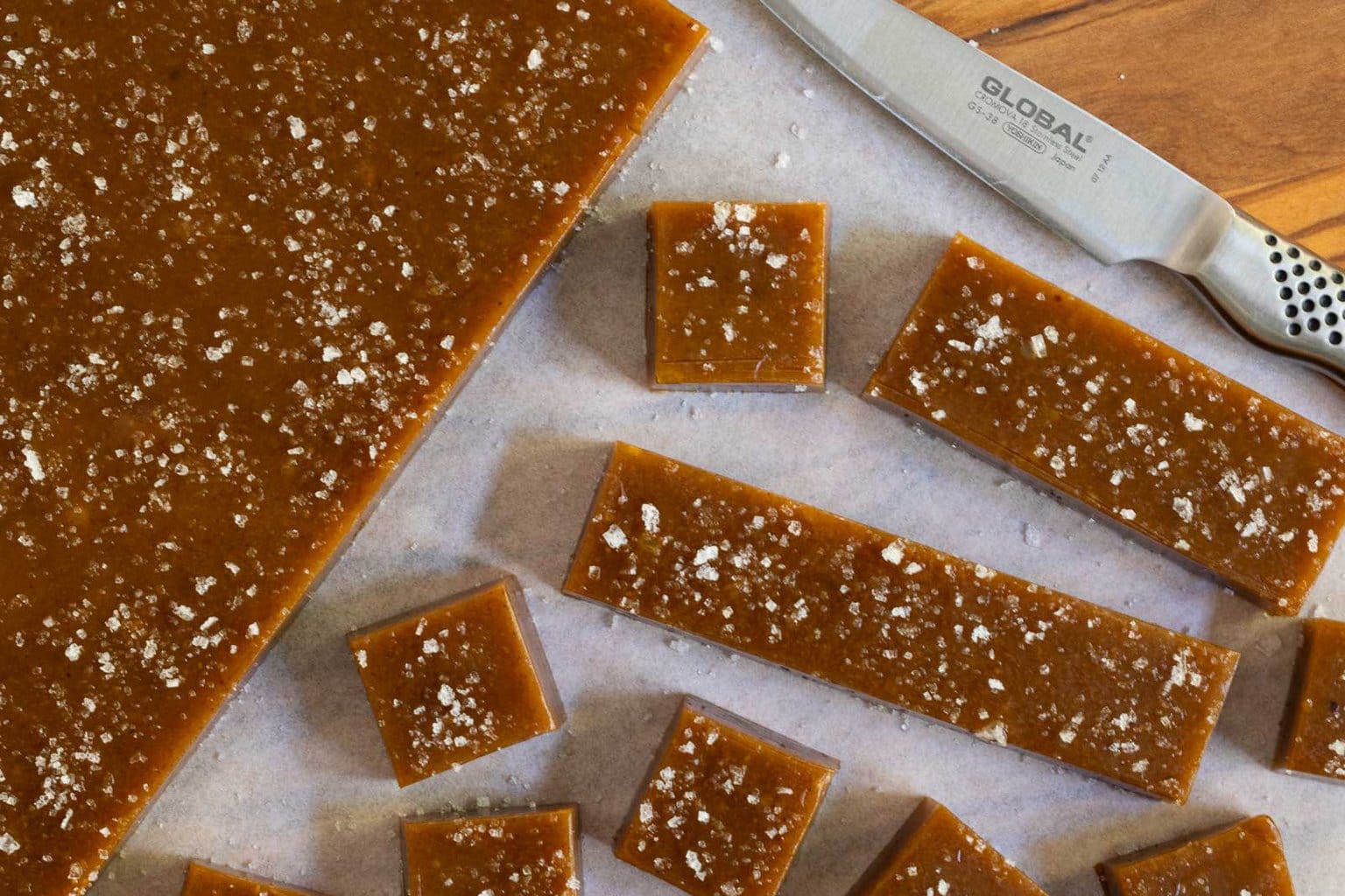 Horizontal overhead closeup photo of the process of cutting Ridiculously Easy Sea-Salted Pumpkin Microwave Caramels into perfect squares.