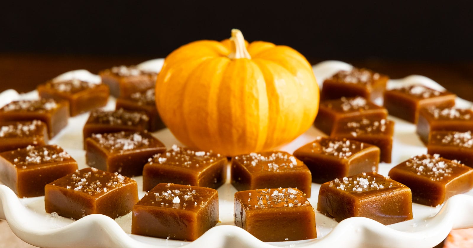 Horizontal photo of a white serving plate of Ridiculously Easy Sea-Salted Pumpkin Microwave Caramels with a mini pumpkin in the center.
