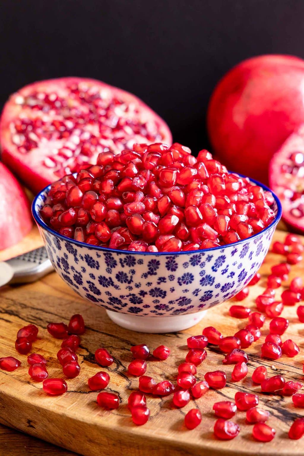 Vertical closeup of a bowl filled with pomegranate seeds surrounded by fresh pomegranates.