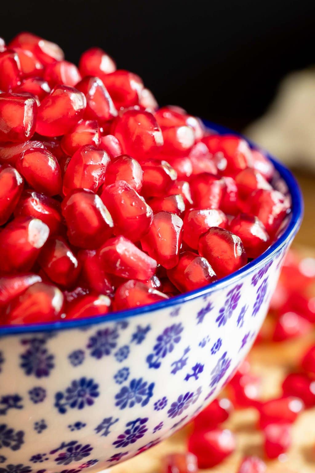 Vertical extreme closeup photo of a white and blue patterned bowl filled with pomegranate seeds.