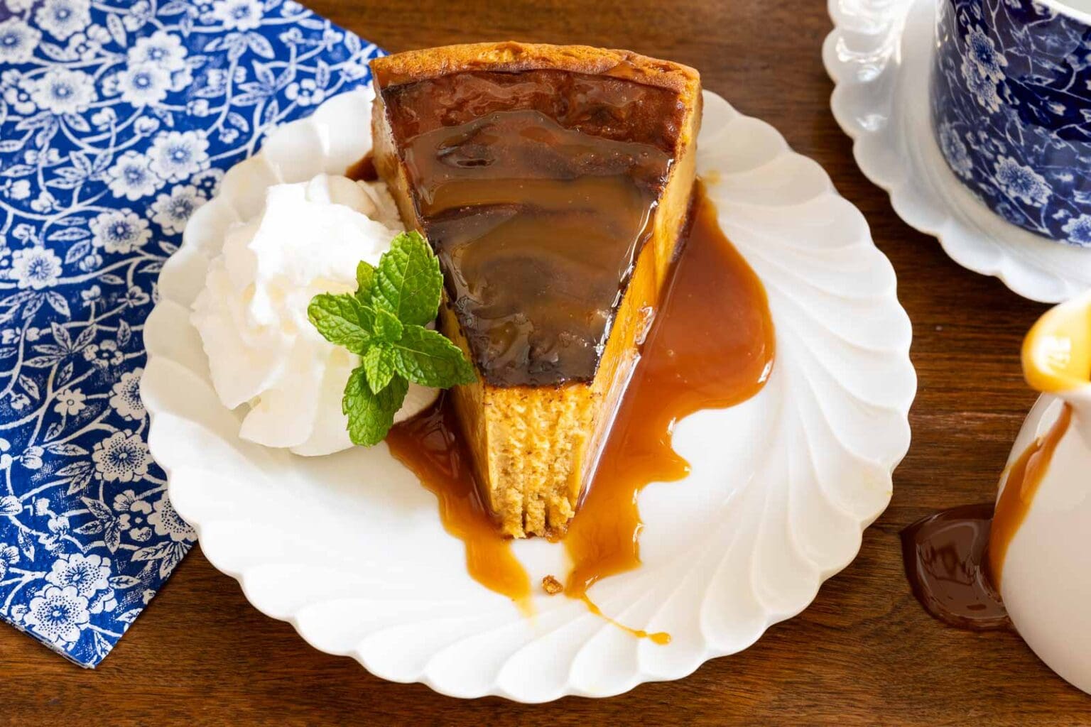 Horizontal closeup photo of a slice of Ridiculously Easy Basque Sweet Potato Cheesecake with caramel sauce on a white serving plate garnished with fresh mint and whipped cream.