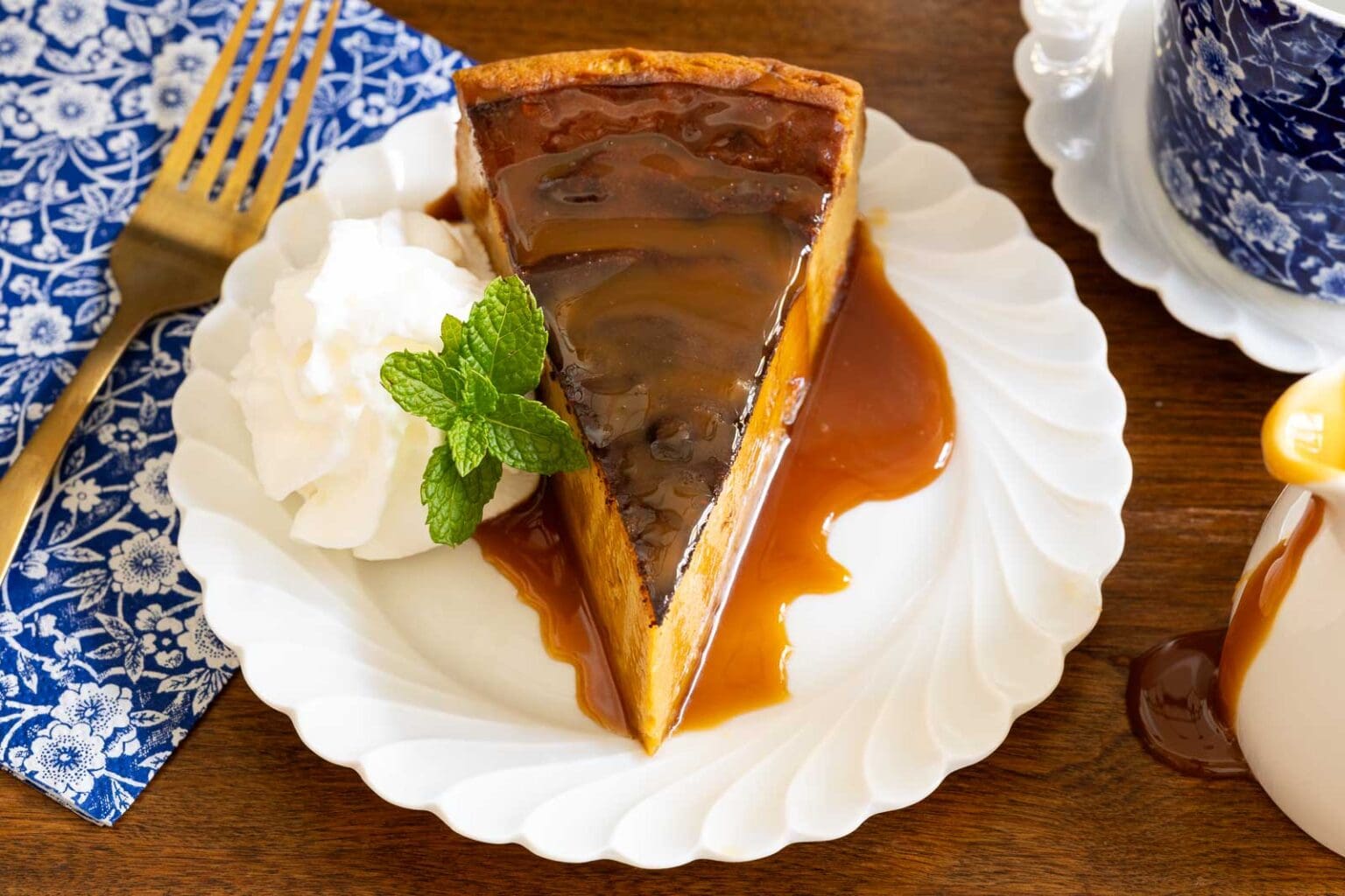 Horizontal closeup photo of a slice of Ridiculously Easy Basque Sweet Potato Cheesecake on a white serving plate garnished with a fresh mint sprig and whipped cream.