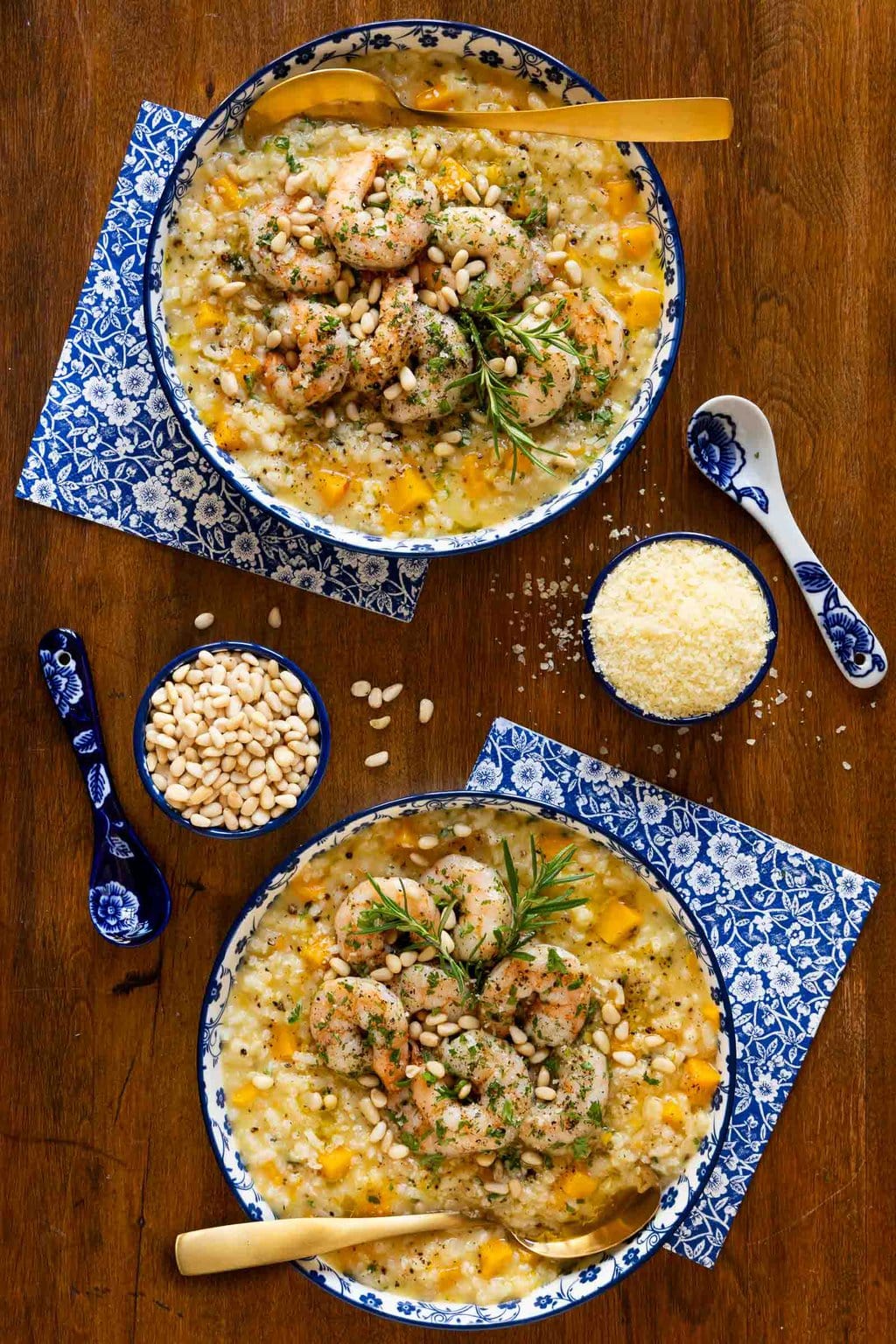 Vertical overhead photo of two blue and white patterned serving dishes of Butternut Squash Risotto with Italian Roasted Shrimp on a wood table.