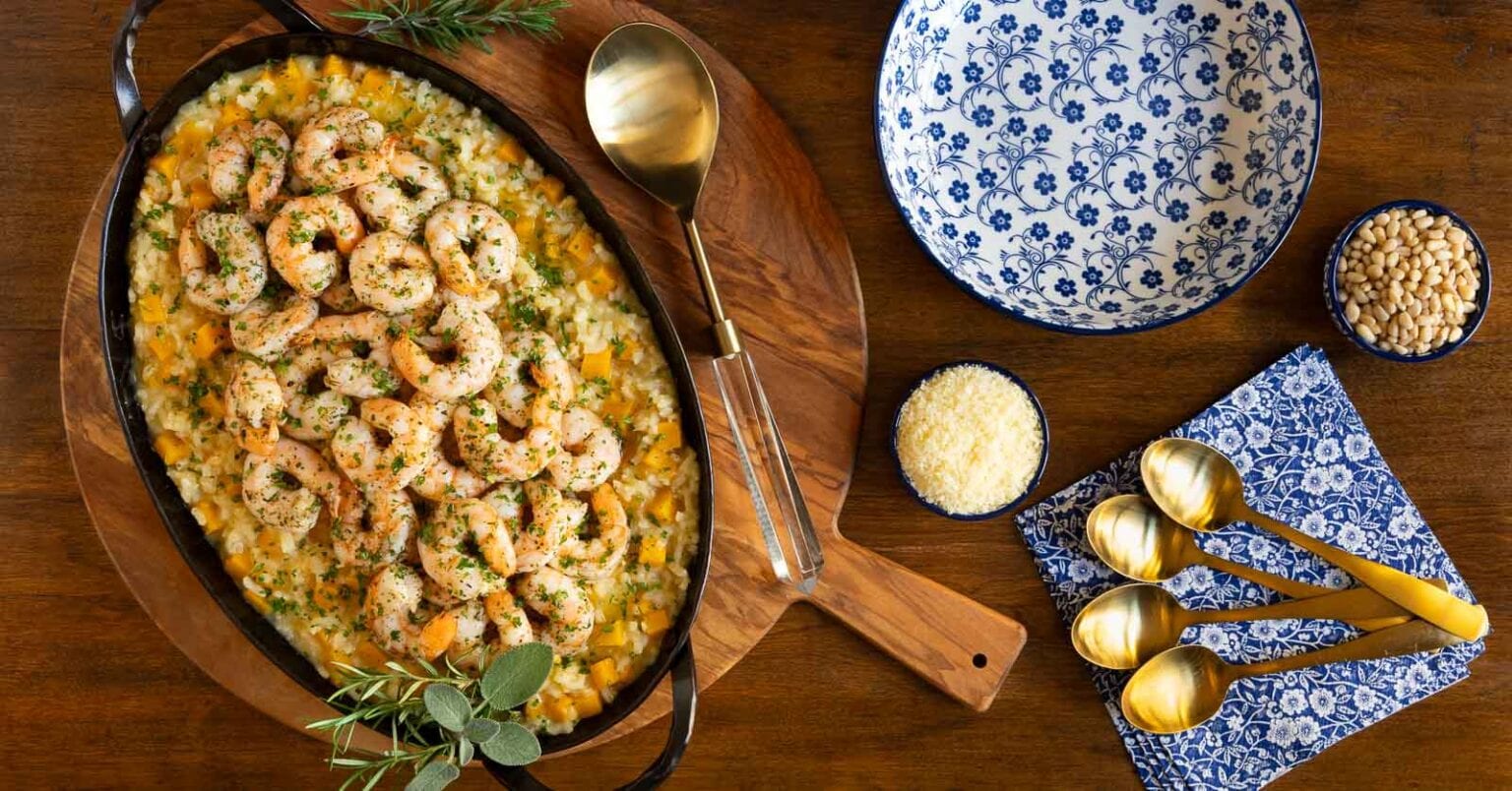 Butternut Squash Risotto with Italian Roasted Shrimp - thecafesucrefarine.com Horizontal overhead photo of a oval steel pan filled with Butternut Squash Risotto with Italian Roasted Shrimp on a round wood platter.