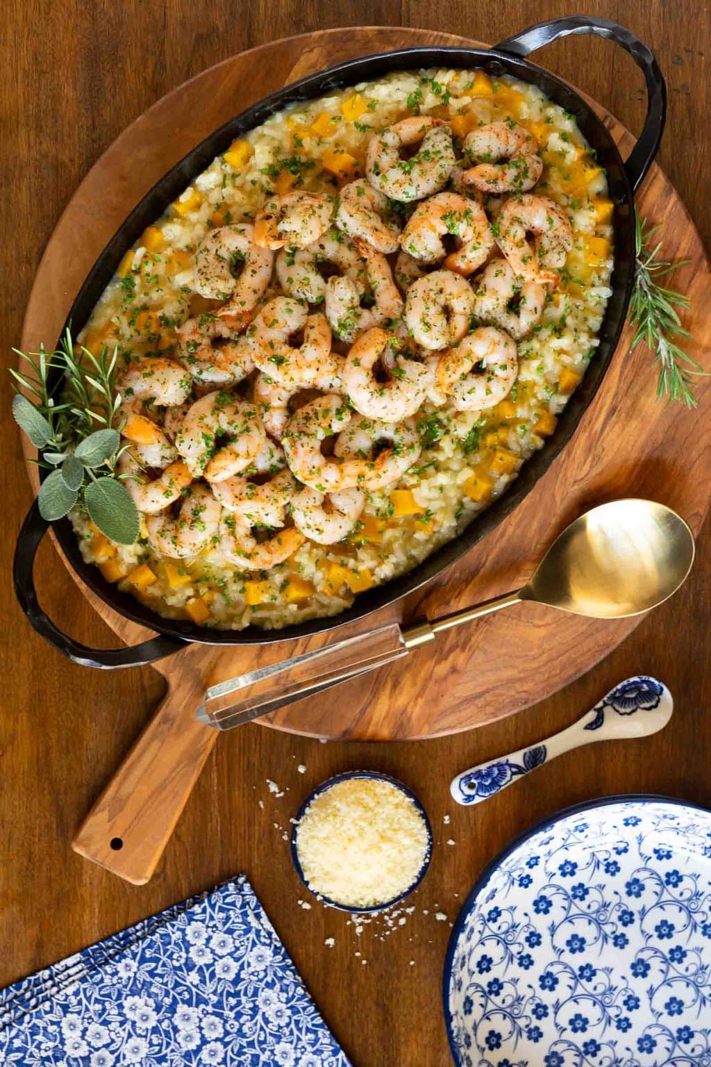 Vertical overhead photo of a hammered steel serving oval dish filled with Butternut Squash Risotto with Italian Roasted Shrimp on a round wood serving plate.