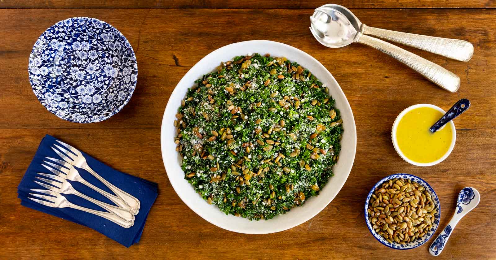 Horizontal photo of a bowl of Pepita Pecorino Kale Salad on a wood table.