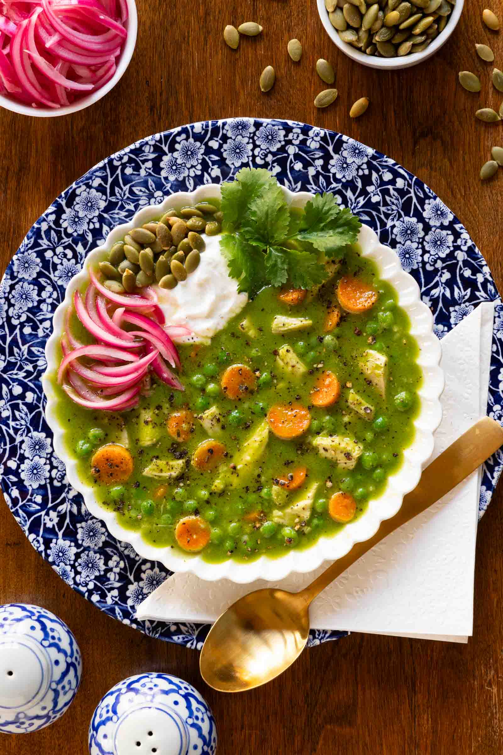 Vertical overhead photo of a bowl of Peruvian Chicken and Rice Soup in white serving bowl garnished with pepitas, pickled red onions, yogurt and cilantro leaves.