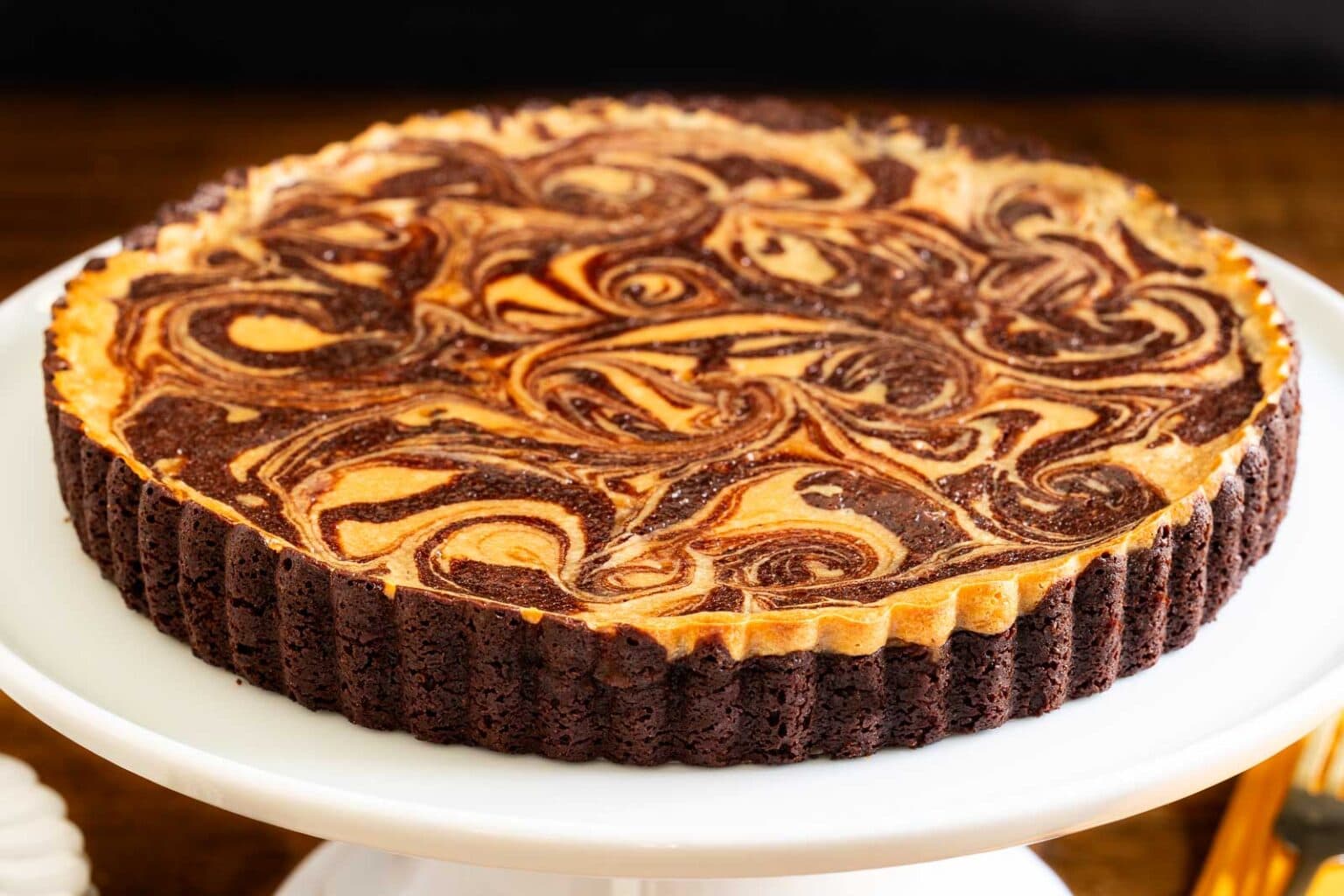 Horizontal closeup photo of a Ridiculously Easy Caramel Cream Cheese Tart on a white pedestal serving plate.
