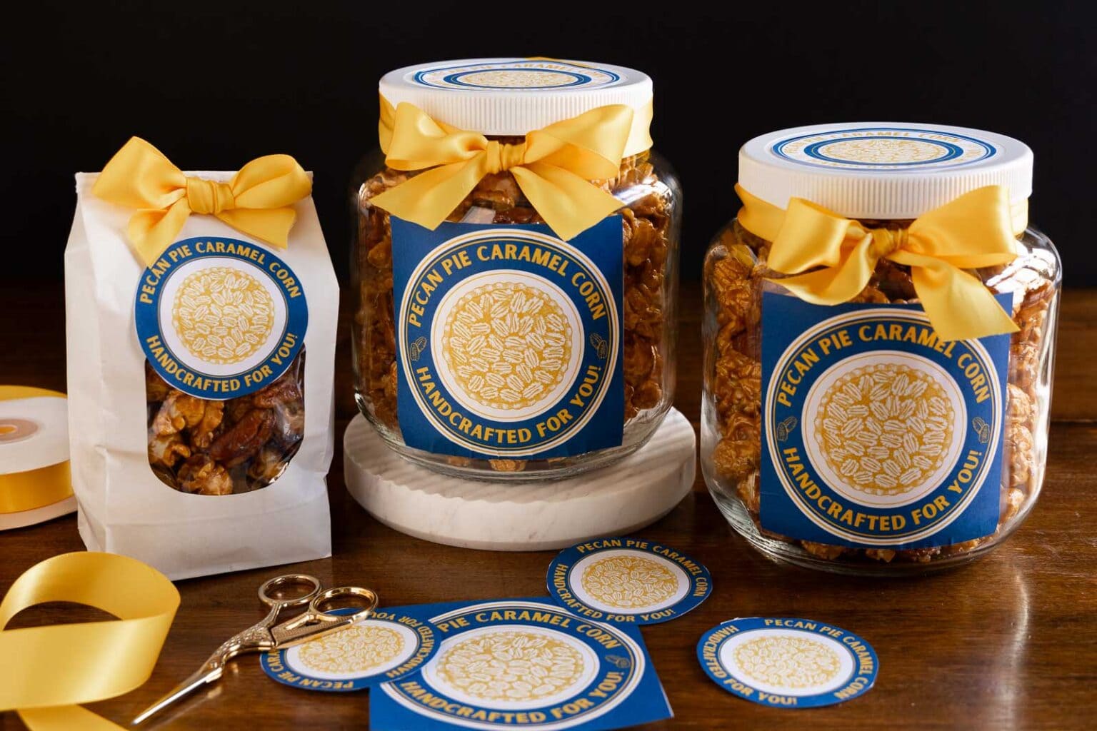 Horizontal photo of jars and a bag of Ridiculously Easy Pecan Pie Caramel Corn with custom labels for gift giving.
