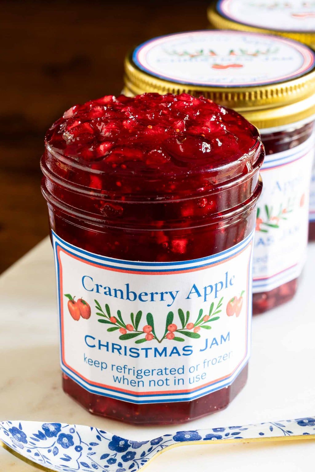 Vertical closeup photo of jars of Cranberry Apple Christmas Jam on a white marble slab