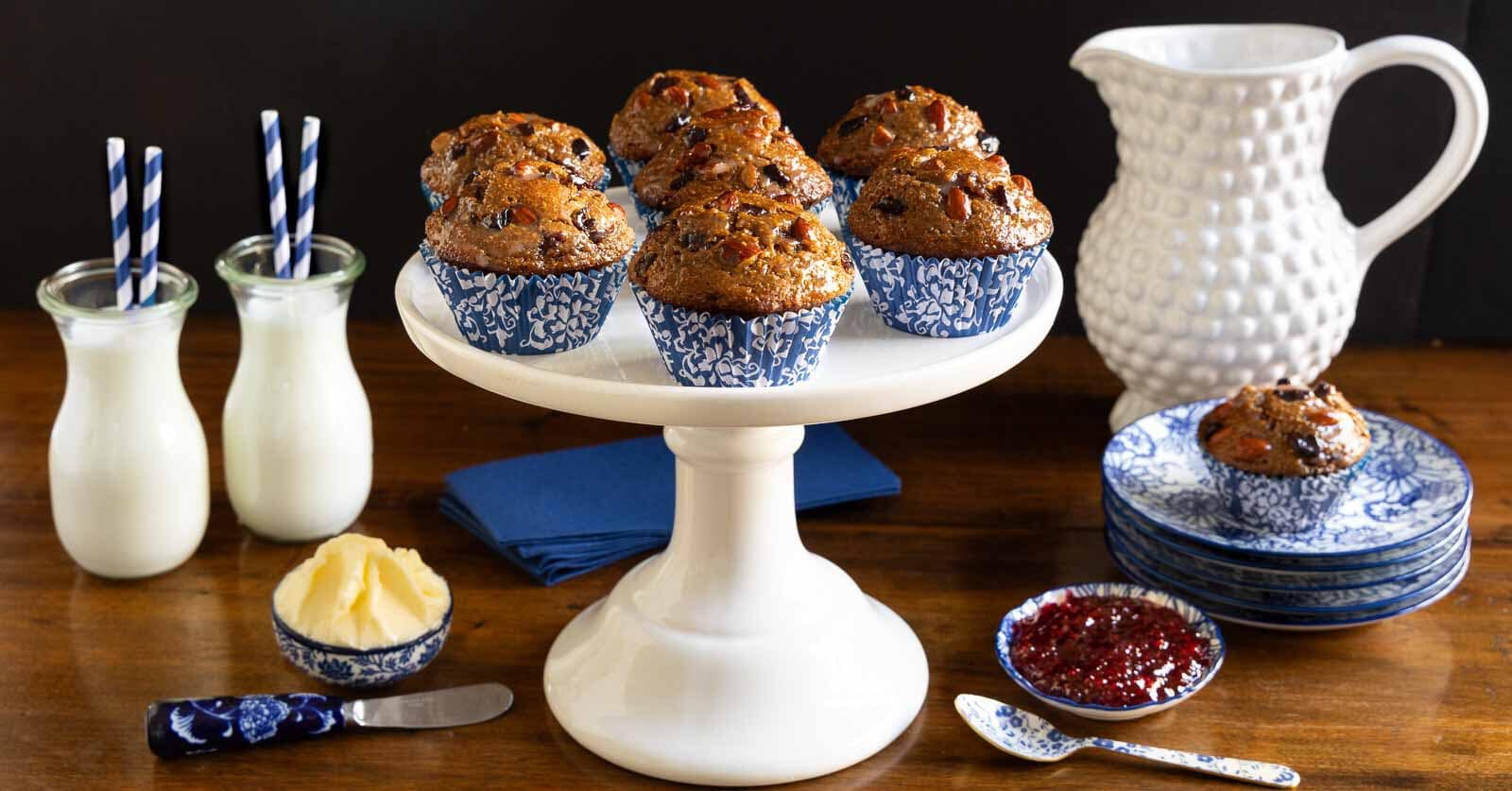 Horizontal photo of a batch of Honey-Glazed Almond Cherry Bran Muffins on a white pedestal serving plate.