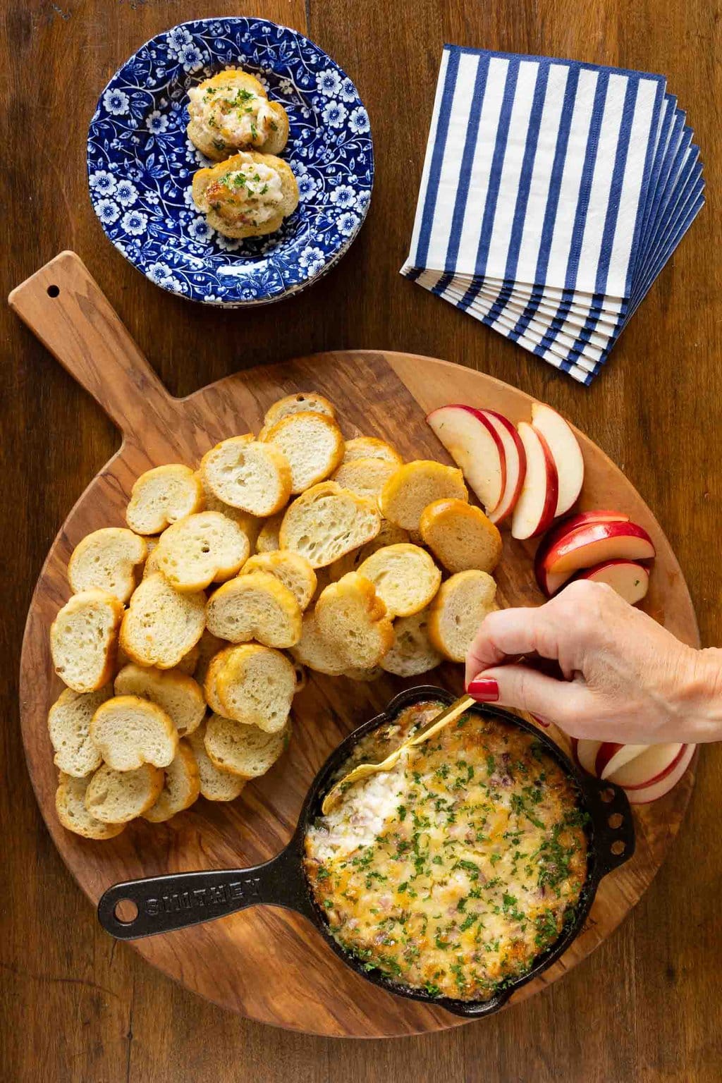 Vertical overhead photo of a cast iron pan of Ridiculously Easy Hot Onion Dip surrounded by apple slices and crostini.