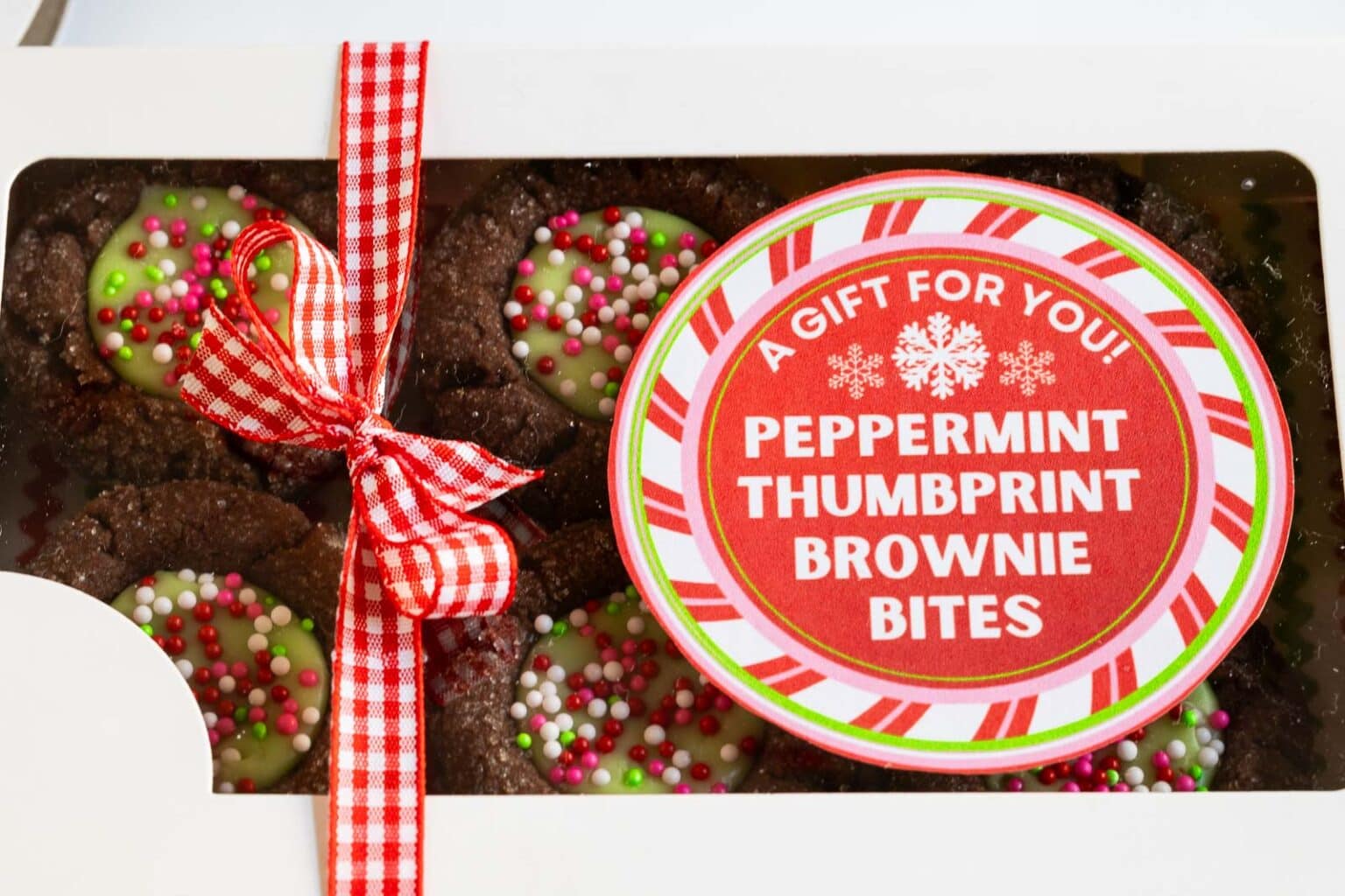 Horizontal extreme closeup photo of a gift box filled with Peppermint Thumbprint Brownie Bites and a custom label for gift giving on top of the box.