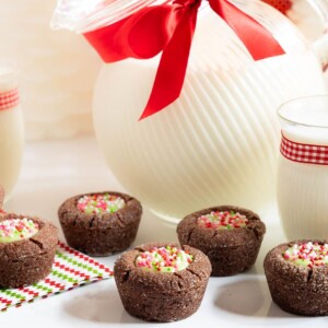 Horizontal closeup photo of a batch of Peppermint Thumbprint Brownie Bites with a jug and glasses of milk in the background.