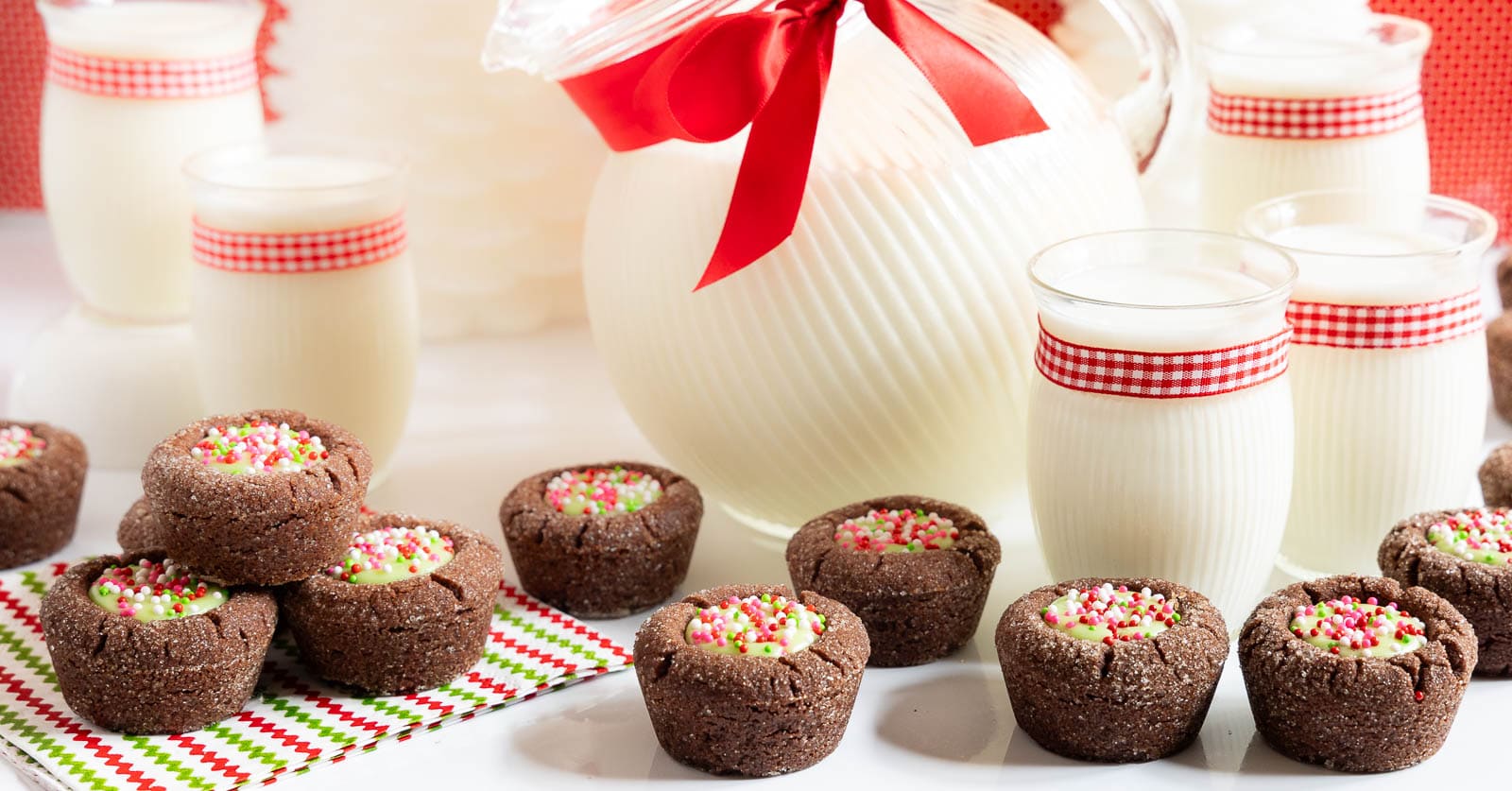 Horizontal photo of a batch of Peppermint Thumbprint Brownie Bites with a jug and glasses of milk in the background.