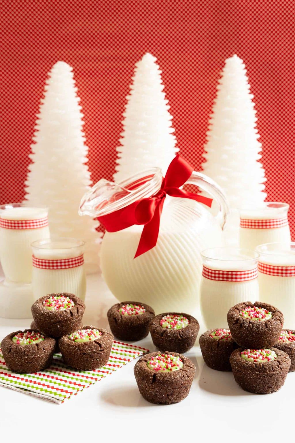 Vertical photo of a batch of Peppermint Thumbprint Brownie Bites with a jug and glasses of milk in the background.