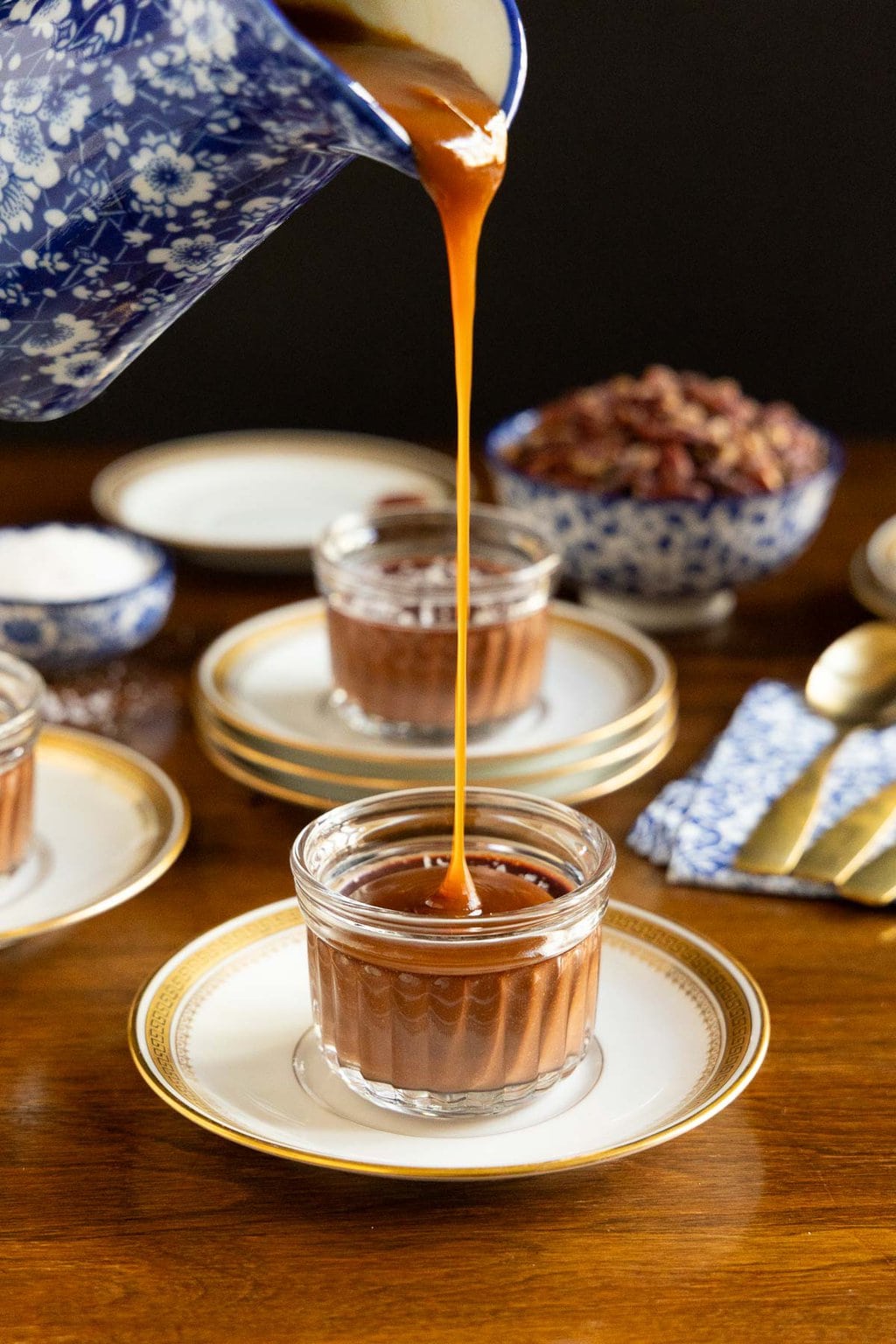 Vertical photo of a pitcher of caramel sauce being poured over a Ridiculously Easy 5 Minute Chocolate Mousse dessert in a glass serving cup.