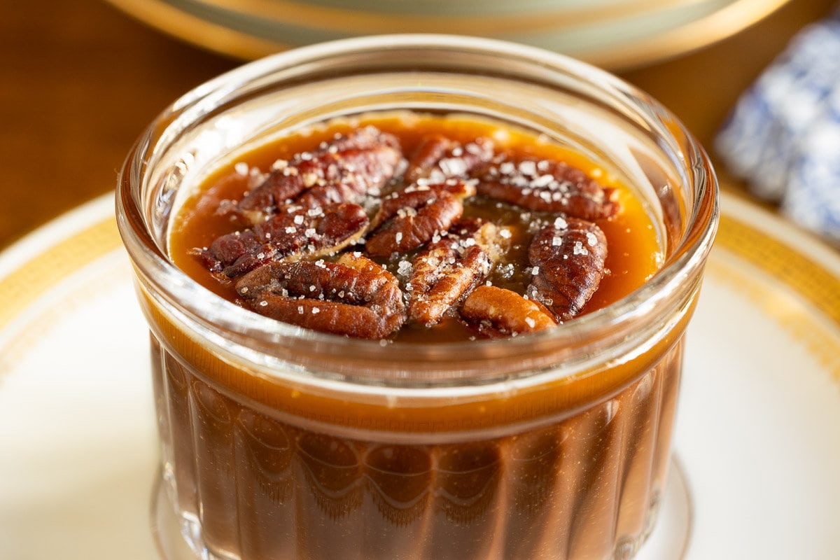 Horizontal extreme closeup photo of a glass serving cup with Ridiculously Easy 5 Minute Chocolate Mousse topped with caramel and butter toasted pecans.