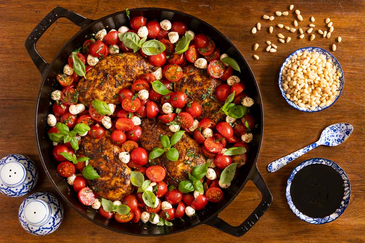 Overhead view of Easy Pan-Seared Chicken Bruschetta with seared chicken breasts, cherry tomatoes, fresh mozzarella pearls, basil, pine nuts, and balsamic glaze in a large skillet.