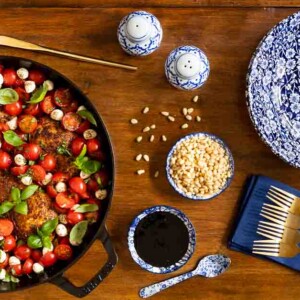 Overhead horizontal photo of a cast iron pan of Easy Pan-Seared Chicken Bruschetta on a wood table garnished with fresh basil leaves and roasted pine nuts.