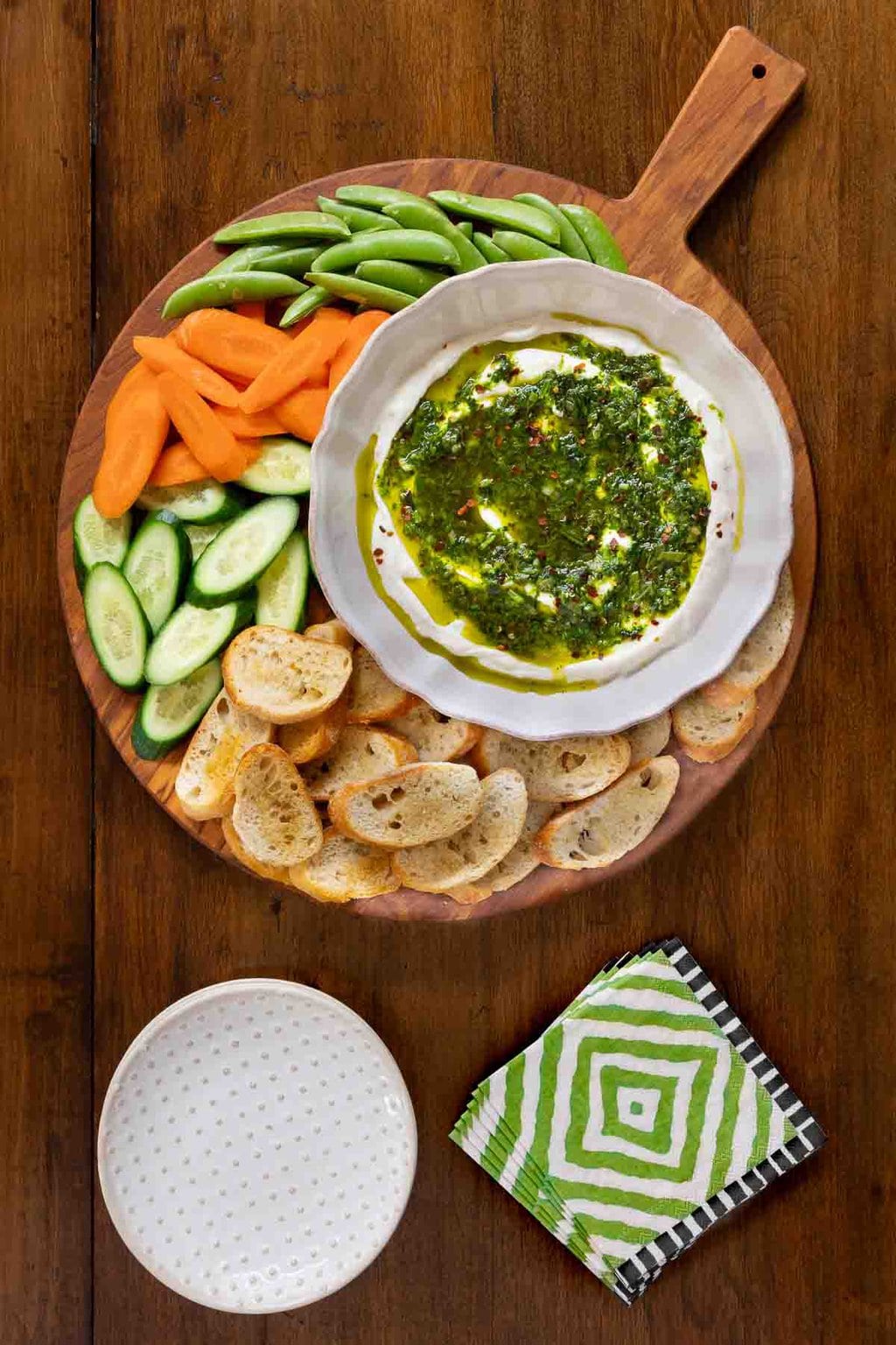 Vertical overhead photo of a wood appetizer filled with vegetables, crostini and Lemony Yogurt Dip with Spicy Herb Oil.