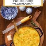Italian Pastina Soup in a Dutch oven on a wooded board with a grater and Parmesan cheese.